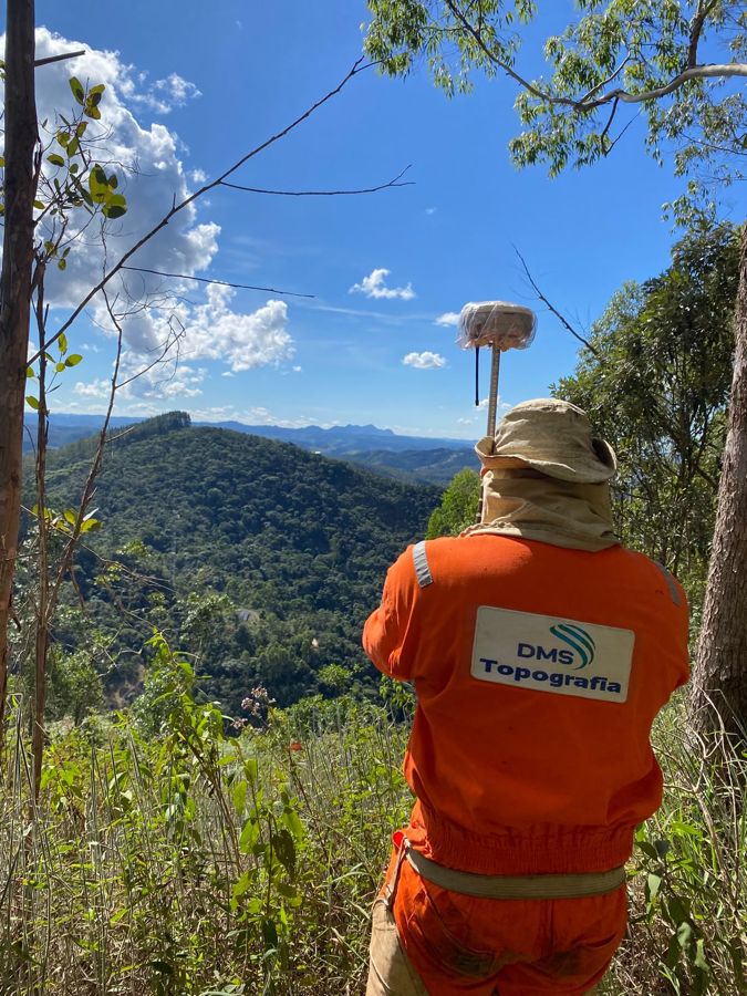 Técnico de costas com uniforme da DMS e receptor GNSS na serra